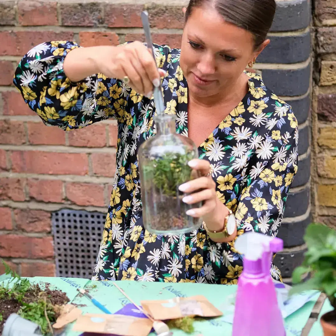 Close‑up of hands layering stones and soil into a glass jar during a date night terrarium session.