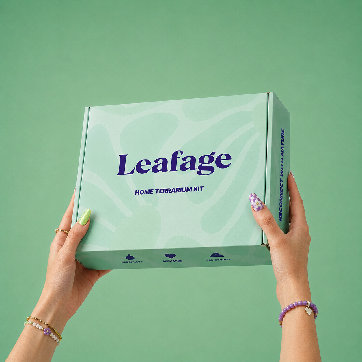 A person holds a mint green box labeled 'Leafage HOME TERRARIUM KIT' against a matching mint green background. The person's hands are visible, adorned with bracelets and patterned nail polish.